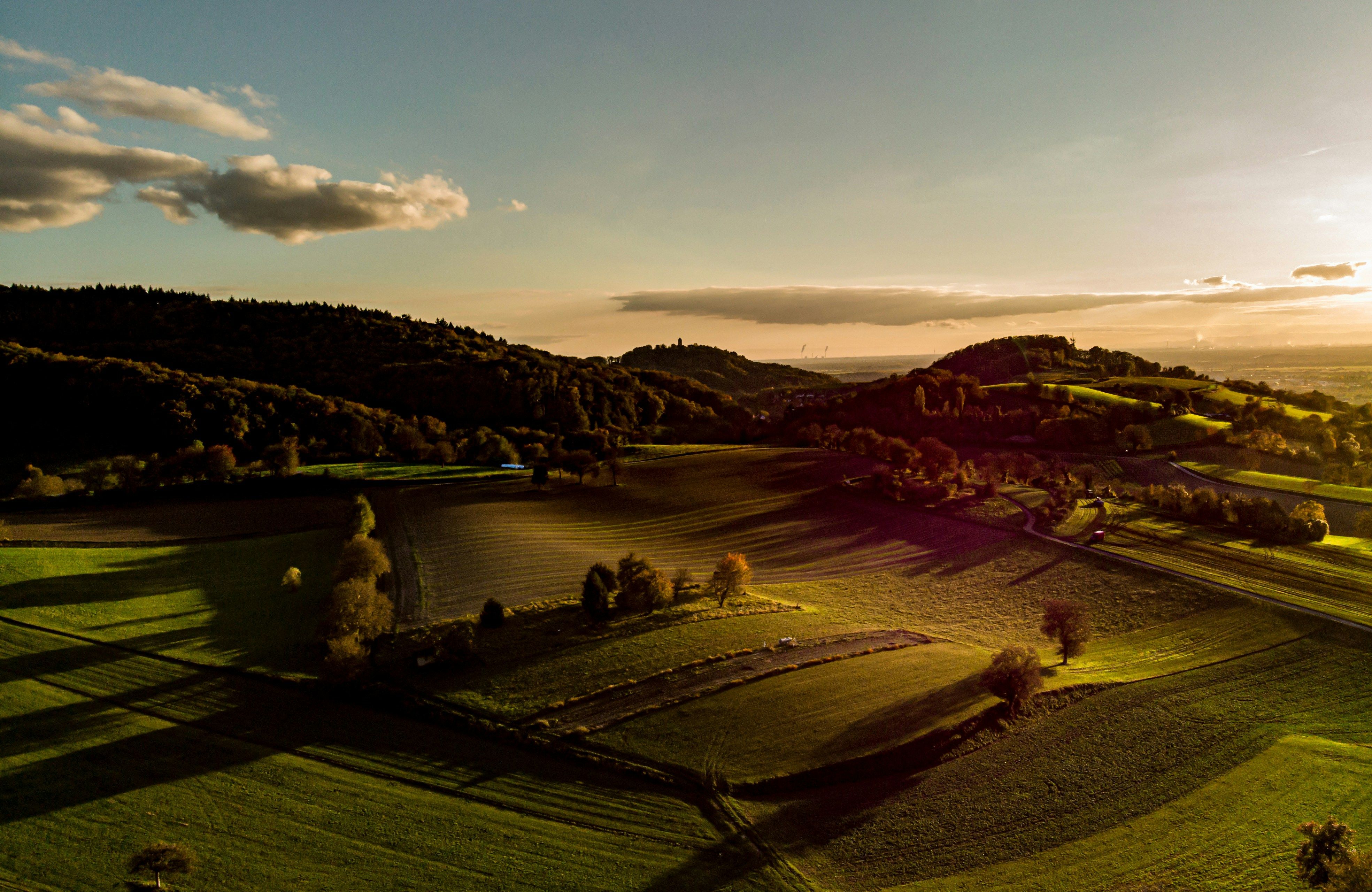 Aerial view of golden hour landscape showing long shadows and warm side lighting creating depth across fields and hills