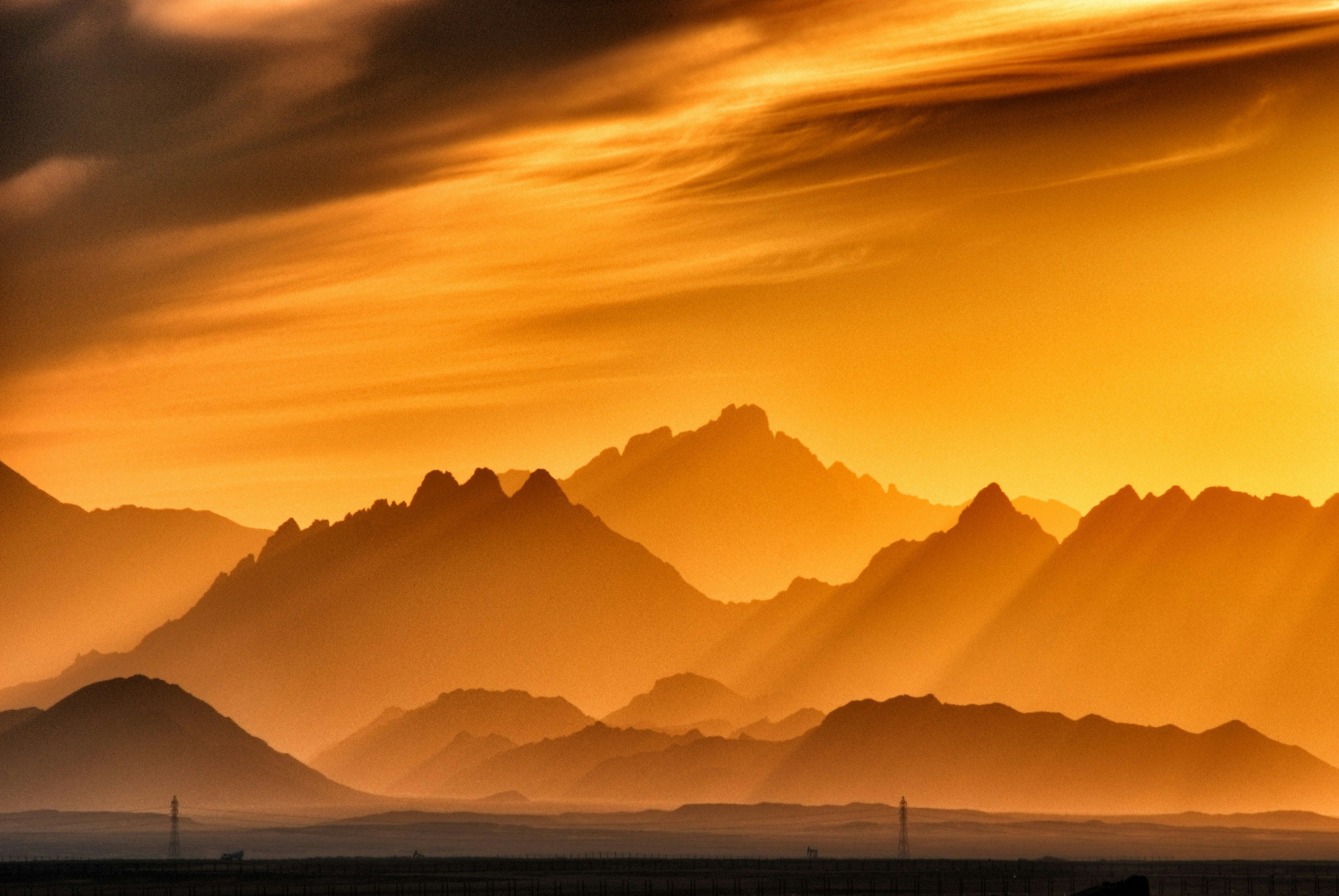 Mountain layers silhouetted in warm golden orange tones during golden hour showing atmospheric haze and rich color temperature