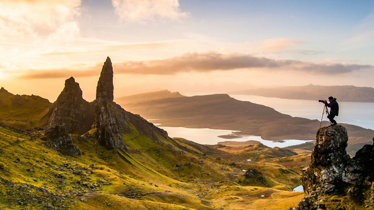 Photographer on a mountain peak shooting golden hour light with scattered clouds at sunset