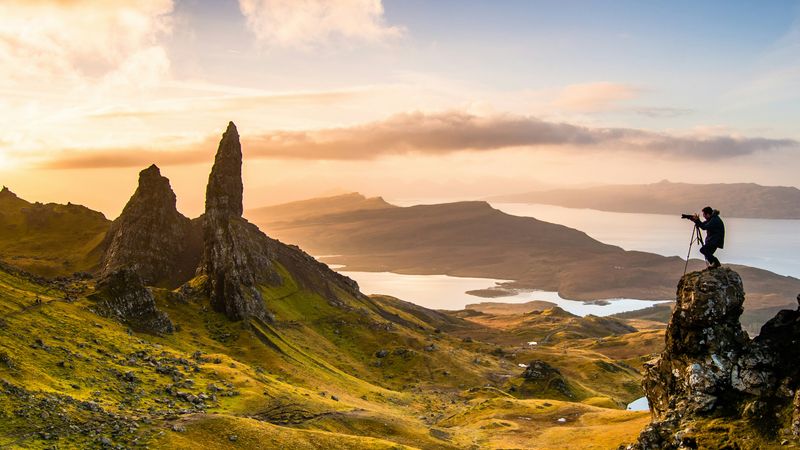Photographer capturing magic hour photography on mountain peak with golden hour light and scattered clouds at sunset